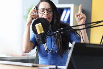 Emotional woman radio presenter in headphones speaks into microphone closeup
