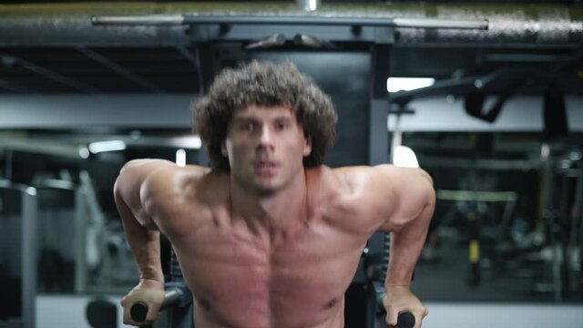 Man exercising on parallel bars. Young athlete exercising in gym. Steadicam shot zoom in.