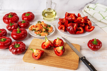 Cutting red ratunda bell peppers into quarters on a wooden chopping board over kitchen table. Preparing raw gogoshar sweet peppers for oven roasting. Seasonal veggies for vegetarian healthy eating.