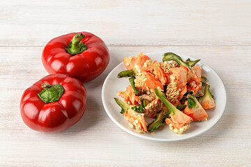 Raw pepper peelings on a white plate and two red ratunda sweet peppers over kitchen table. Heap of organic gogoshar bell peppers peels close-up. Household biodegradable kitchen waste for recycle.