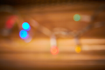 Abstract Christmas string of fairy lights on warm brown wood shelf background blurry defocused with multi coloured light bulb bokeh copyspace