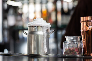 Milkshake with foam in metallic jar isolated on bar background