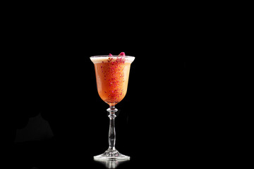 Glass with orange cocktail decorated with dried rose on the bar on a black background. the drinks is decorated with flower