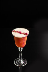 Glass with orange cocktail decorated with dried rose on the bar on a black background. the drinks is decorated with flower