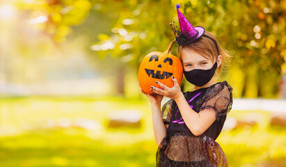 Portrait blonde girl in witch costume with pumpkin in her hands. Halloween kids wearing mask.