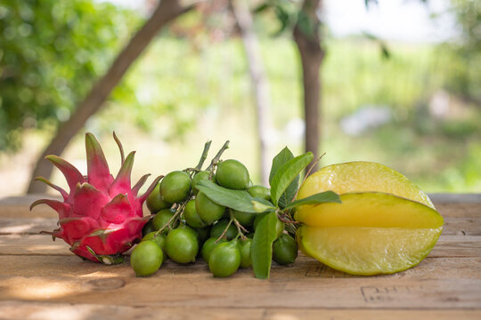 EXOTIC TROPICAL FRUITS SUCH AS QUENEPA, MAMONCILLO OR LIMONCILLO, PITAHAYA OR DRAGON FRUIT, PASSION FRUIT OR MARACULLA AND CARAMBOLA ON OUTDOOR WOODEN TABLE WITH NATURAL LIGHT AND UNFOCUSED BACKGROUND
