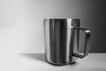 Gray shinny metal cup with a handle on white background. Food and eating utensils still live for an abstract theme with space for text and a simple, minimalist design.