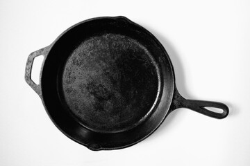 Rustic black iron pan oiled and dried. High contrast metal cooking tool still life on white background.