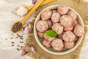 Frozen meatballs with spices, basil leaves, and garlic cloves in a ceramic bowl