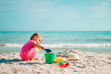 A little girl plays with a shoulder blade and a bucket on the beach in a pink heart dress