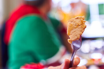Piece of roast turkey on a fork held in a white mans hand. Negative space for text copy. Woman wearing red & green christmas shirt in background blurred shallow depth of field