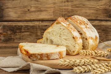 Freshly baked bread with wheat ears, fragrant pieces on a cutting board