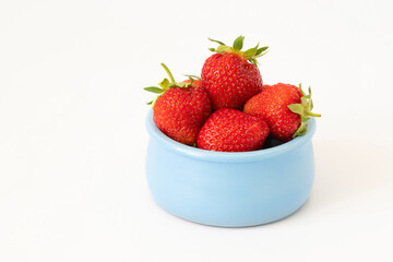 Fresh juicy strawberries in a blue bowl on a white background with a copy space. Red ripe berries in a dish close up.