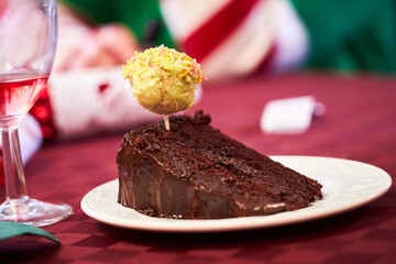 Slice of chocolate fudge cake garnished with cake pop being eaten with a spoon on a red tablecloth for christmas