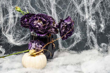Spooky, Halloween display of dark purple flowers with a white pumpkin. background with cob webs. 