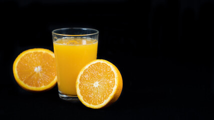 Glass of freshly squeezed orange juice, halved orange and strawberries, on black background