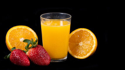 Glass of freshly squeezed orange juice, halved orange and strawberries, on black background