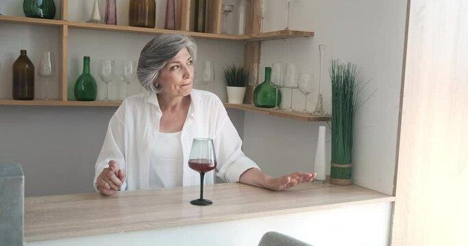 An elderly woman drinking wine in the kitchen and dancing, enjoying the singlehood and freedom of old age.