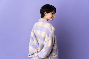 Woman with short hair isolated on purple background in back position and looking back