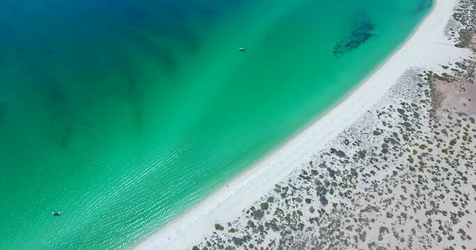 Descending Flight to Large Desert Waterfront Beach with Distant Anchored Sailboats

