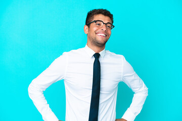 Young business Brazilian man isolated on blue background posing with arms at hip and smiling