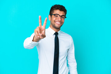 Young business Brazilian man isolated on blue background smiling and showing victory sign