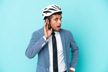 Young business Brazilian man with bike helmet isolated on blue background listening to something by putting hand on the ear