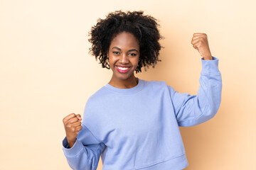 Young African American woman isolated on beige background celebrating a victory
