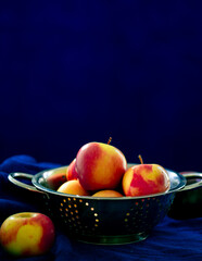 Fresh orangish color apples in a colander against blue background.