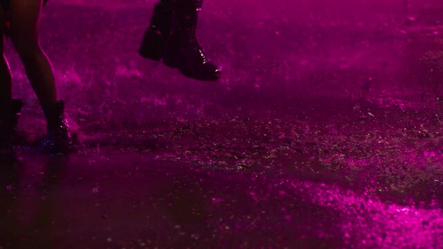 Footage of young people's feet and legs jumping and dancing in the rain at night. 