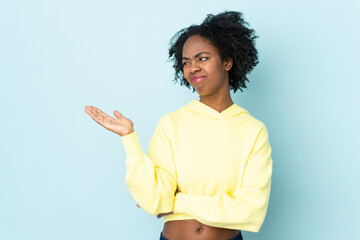 Young African American woman isolated on blue background holding copyspace with doubts