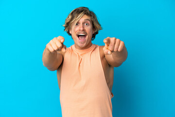 Naklejka premium Handsome blonde man isolated on blue background surprised and pointing front