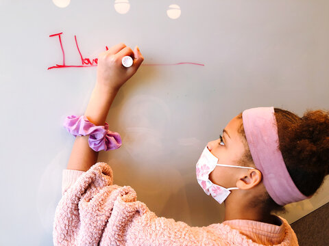 Young girl wearing a mask writing on a whiteboard