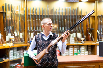 Portrait of focused man inspecting sporting shotgun in gunsmith shop