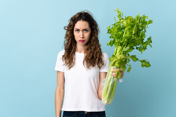 Young woman holding a celery isolated on blue background with sad expression