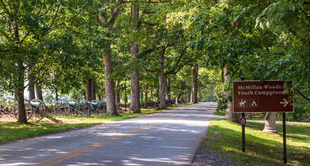 West Confederate Avenue in the Gettysburg National Military Park lined with trees and civil war cannons along with a sign for McMillan Woods Youth Campground on a sunny summer day