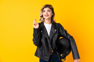 Teenager woman holding a motorcycle helmet isolated on yellow background with fingers crossing