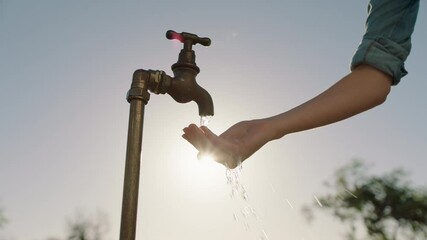 farmer woman washing hand under tap on rural farm freshwater flowing from faucet with afternoon sun flare