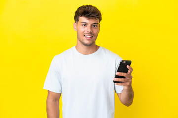 Young caucasian handsome man isolated on yellow background using mobile phone