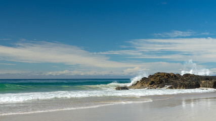 A view of a sandy beach, waves breaking over rocks and clouds on the horizon at Currumbin Beach, Gold Coast, Queensland, Australia. 