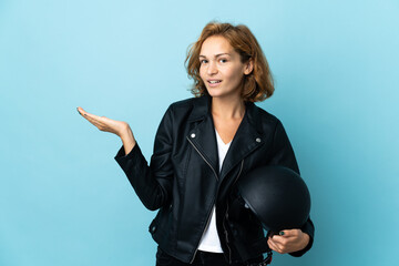 Georgian girl holding a motorcycle helmet isolated on blue background extending hands to the side for inviting to come