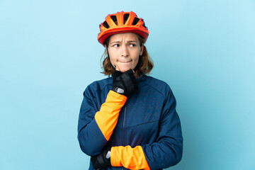 Young cyclist woman isolated on blue background having doubts and thinking