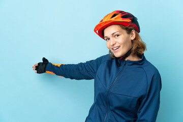 Young cyclist woman isolated on blue background extending hands to the side for inviting to come