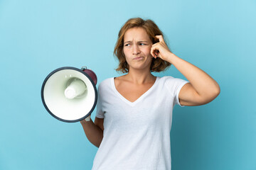 Young Georgian woman isolated on blue background holding a megaphone and having doubts