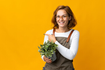 Young Georgian woman holding a plant isolated on yellow background pointing to the side to present...