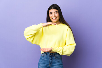 Young brunette woman over isolated purple background holding copyspace imaginary on the palm to insert an ad