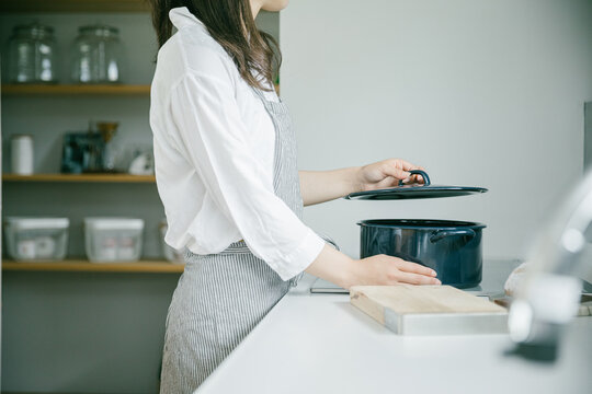 きれいなキッチンで女性が一人鍋の蓋を持ち上げている　woman kitchen