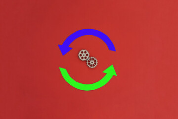 Two wooden gears, two round blue and green arrows on a red background.  The concept of movement, interaction.