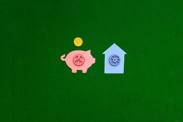 Piggy bank, gear house on a green background. The housing market. Purchase, sale of non-movable property.