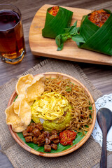 Nasi Kuning with a glass of tea and rice packaged with banana leaf photographed on wooden table